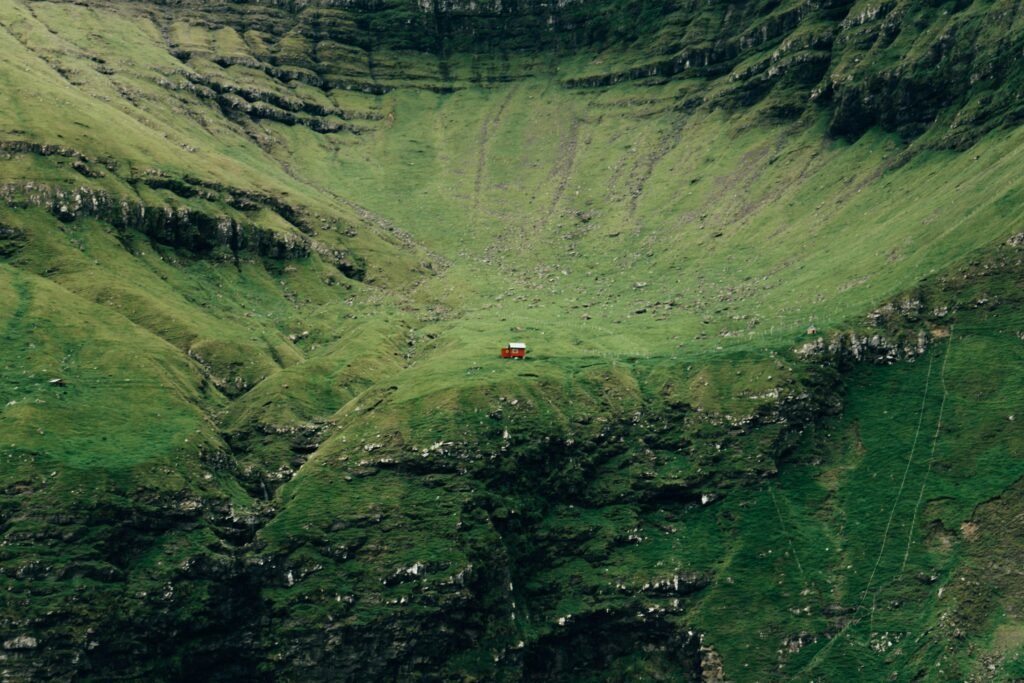 Explore the serene beauty of a lone red house nestled in the verdant green hills of the Faroe Islands.